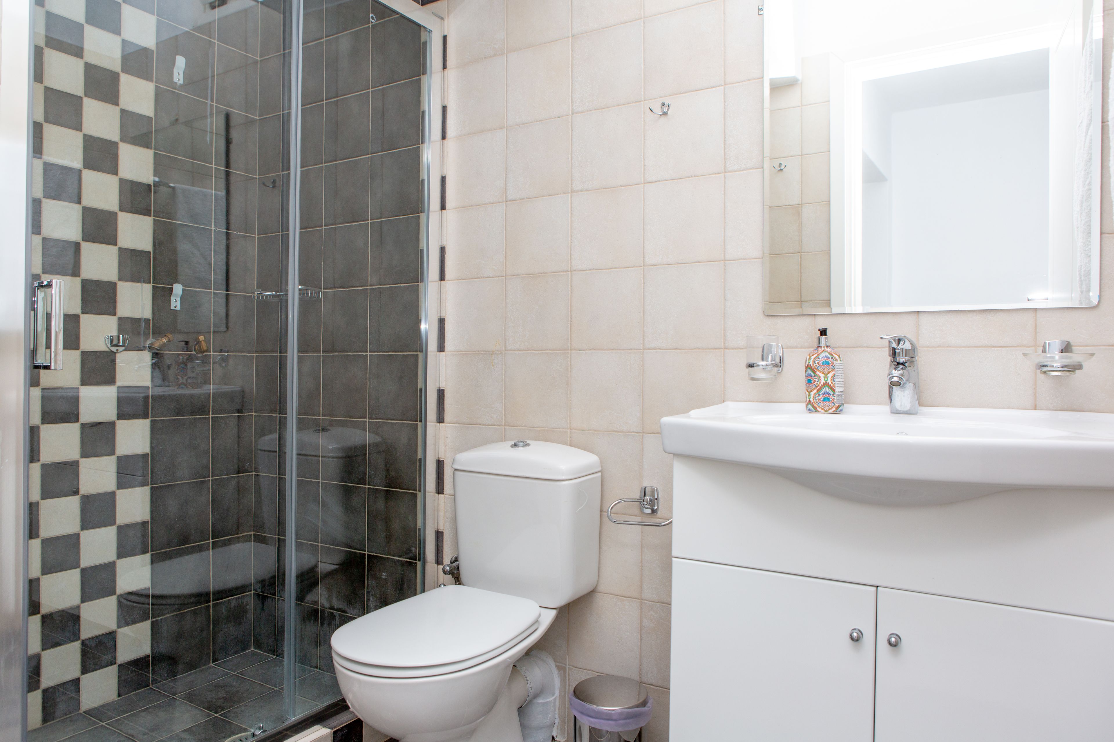 A bathroom with a glass shower enclosure, a toilet, and a sink with a mirror above it.