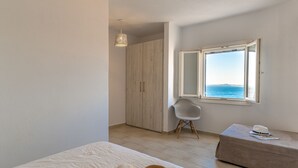 Een slaapkamer met een groot raam, een kledingkast, een nachtkastje met een hoed erop, en een open boek.