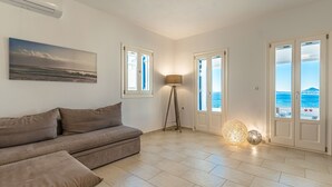 Een ruime woonkamer met een beige bank, een vloerlamp en een schilderij van een strandlandschap.