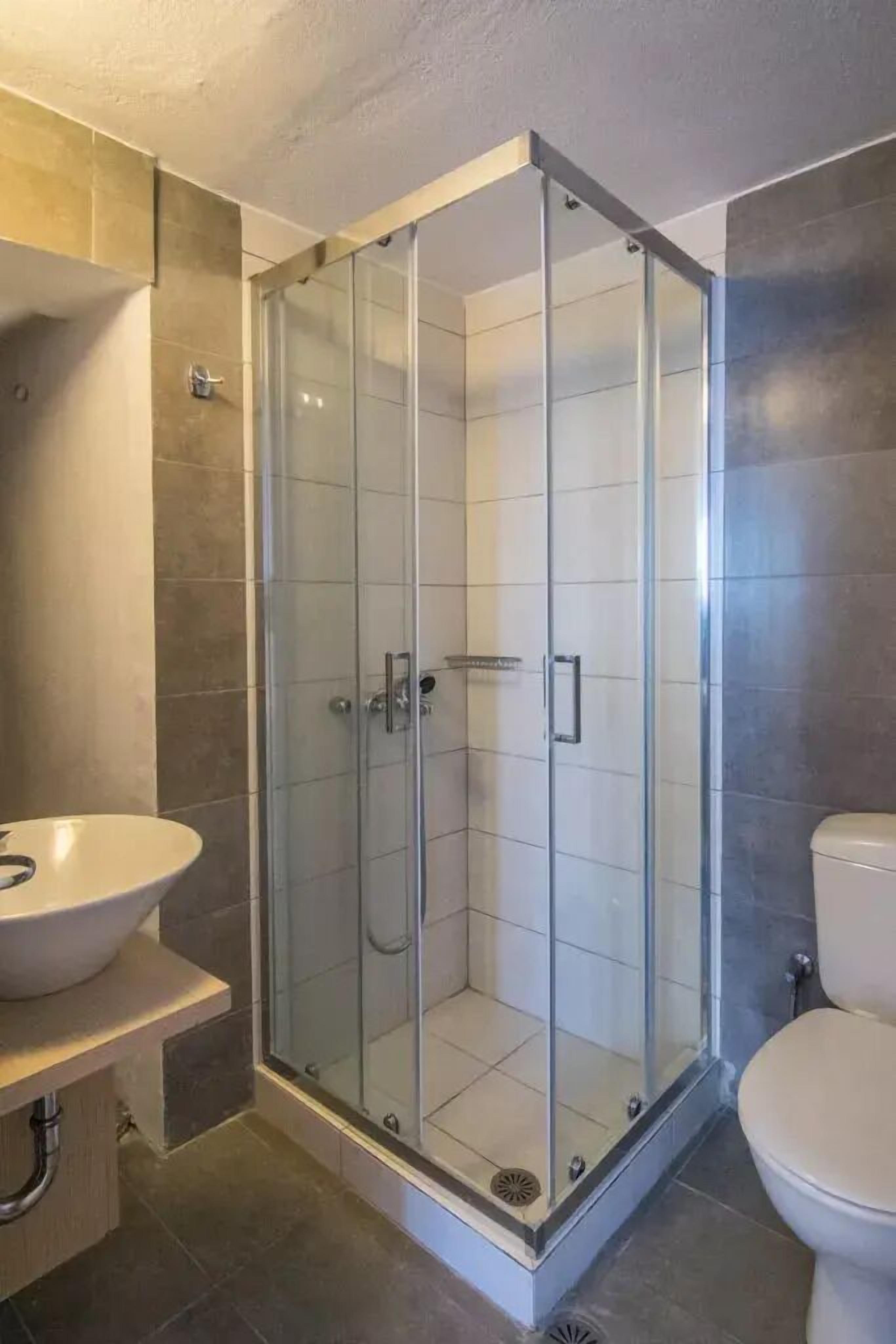 A modern bathroom with a glass-enclosed shower, a white sink, and a toilet.