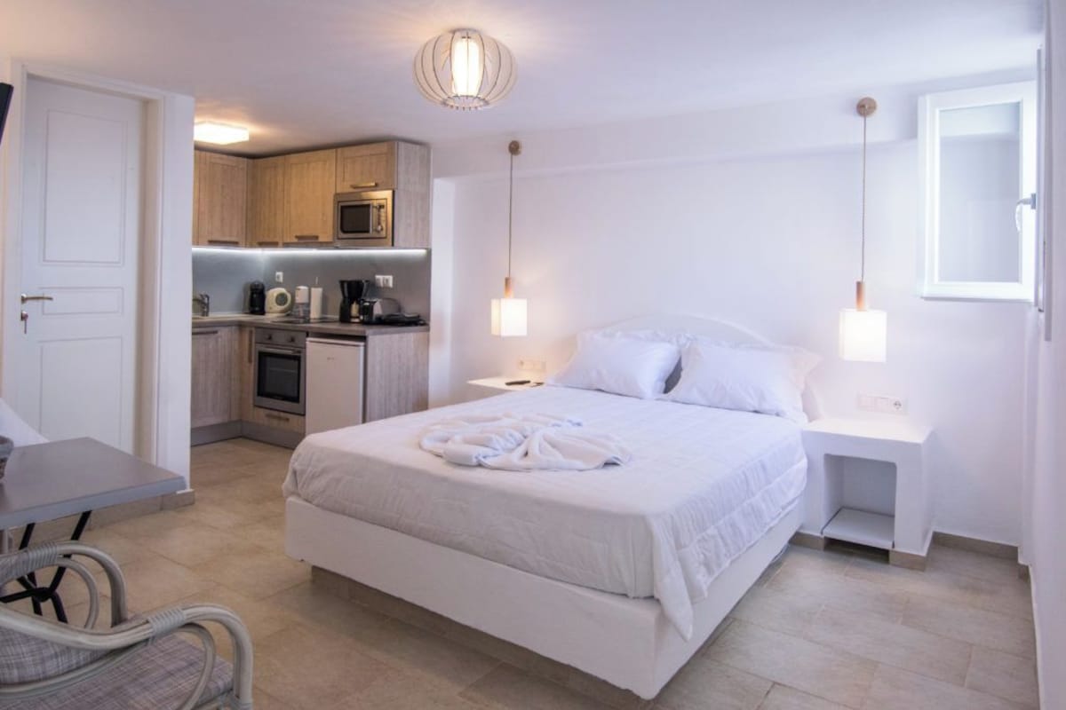 Een hotelkamer met een bed, nachtkastjes, een bureau, een stoel, een kitchenette en een badkamer.