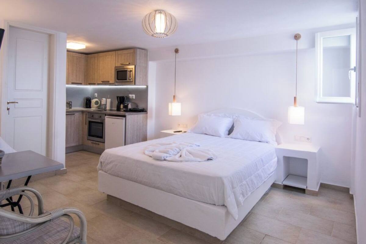 Een hotelkamer met een bed, nachtkastjes, een bureau, een stoel, een kitchenette en een badkamer.