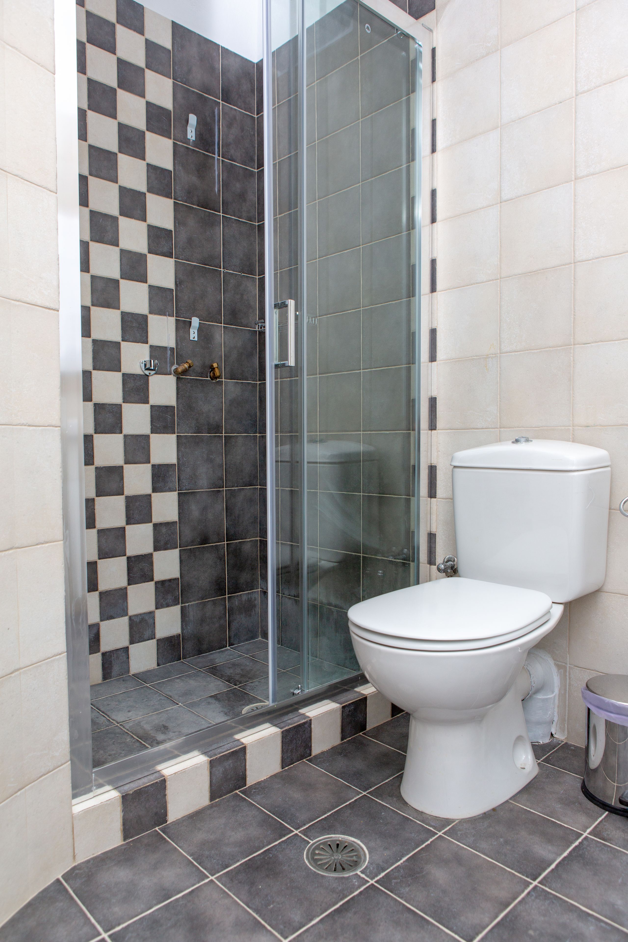 Een badkamer met een douchecabine van glas, een wit toilet en wandtegels in ruitpatroon.