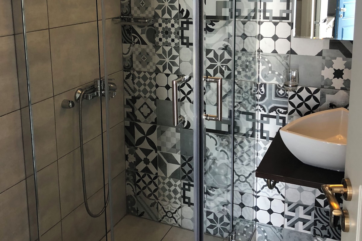 Een moderne badkamer met tegelvloeren met een patroon, een glazen douchecabine en een wastafel met een zwart aanrecht.