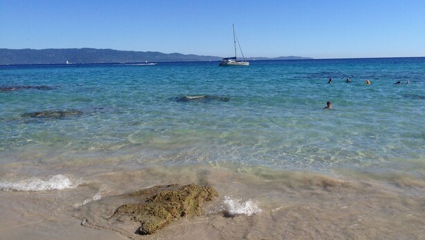 A beach with clear water, a sailboat, and people swimming. - Magnificent sea view More than 50 star reviews from my hosts !!! (Ajaccio)