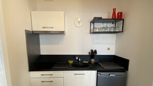 A compact kitchen with a black countertop, white cabinets, a black dishwasher, and a small shelf with glassware. - Magnificent sea view More than 50 star reviews from my hosts !!! (Ajaccio)