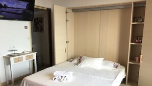 A neatly arranged hotel room with a bed, a television mounted on the wall, a small desk with drawers, and a wardrobe with a mirror. - Magnificent sea view More than 50 star reviews from my hosts !!! (Ajaccio)