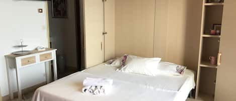 Habitación de hotel ordenada con cama, televisor montado en la pared, escritorio pequeño con cajones y armario con espejo.