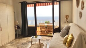 A room with a sofa, a small table, a chair, and a view of the sea through a sliding door. - Magnificent sea view More than 50 star reviews from my hosts !!! (Ajaccio)