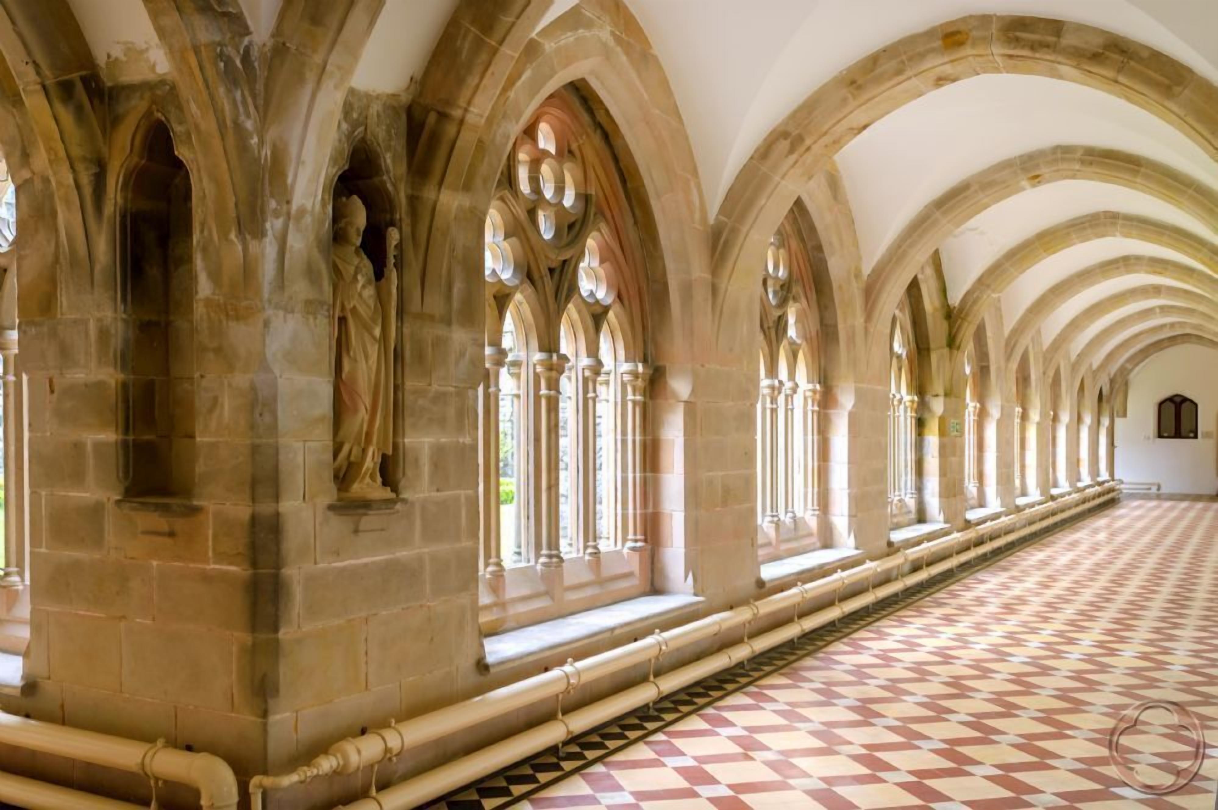 A corridor with arched ceilings and stone walls, featuring a checkered floor pattern.