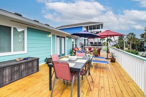 Eine Holzterrasse mit Tisch, Stühlen und Sonnenschirmen sowie einer Bank.