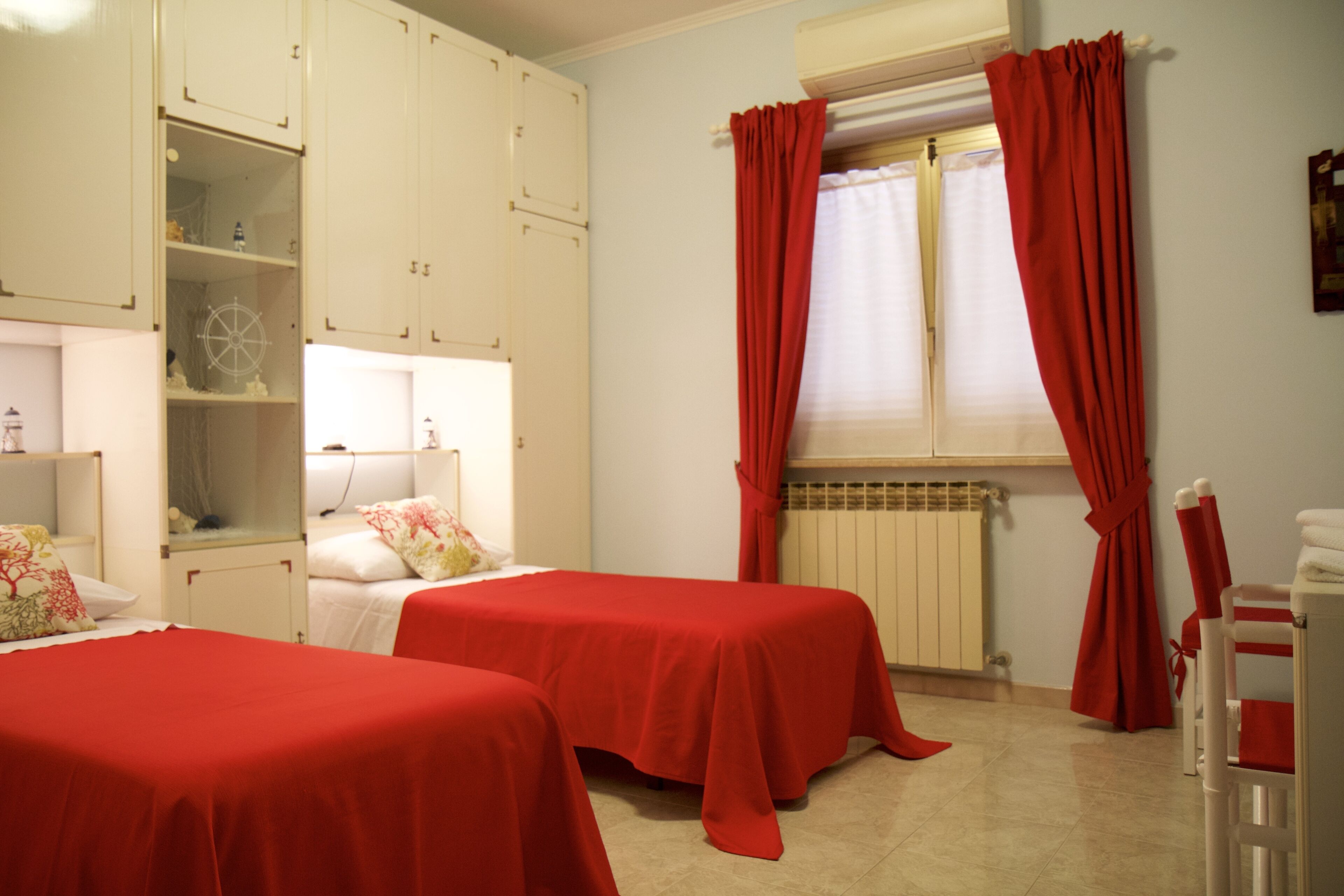 A room with two beds, a radiator, and a window with red curtains.