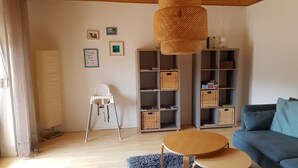 A living room with a blue sofa, a wooden coffee table, a white chair, and a bookshelf filled with wicker baskets. - Apartment Betula, near Pullman City in the district of Passau in the Bavarian Forest (Fürstenstein)