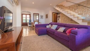A living room with a purple sofa, a wooden TV stand, a staircase, and a dining area.