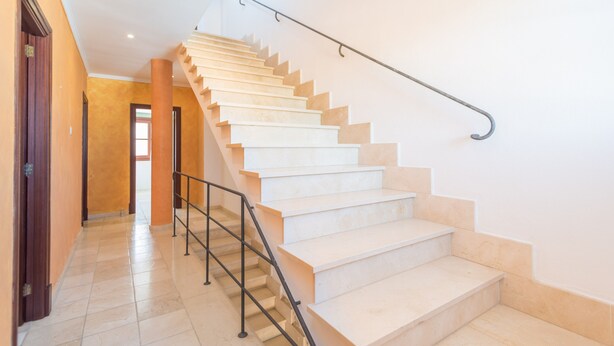 A staircase with a metal handrail, leading to a landing with a door.