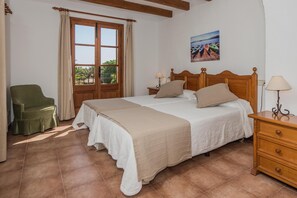 A bedroom with a large bed, a wooden nightstand, a green armchair, and a window with curtains. - Mastaguera Mallorcan style villa with pool and spectacular views (Pollença)