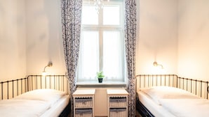 A room with two single beds, a window with curtains, a radiator, and a small table with baskets. - Beach Love - Villa on the beach (Heringsdorf)