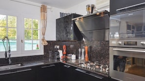 A modern kitchen with dark cabinetry, stainless steel appliances, and a window with a view of greenery. - villa near cannes (Mougins)
