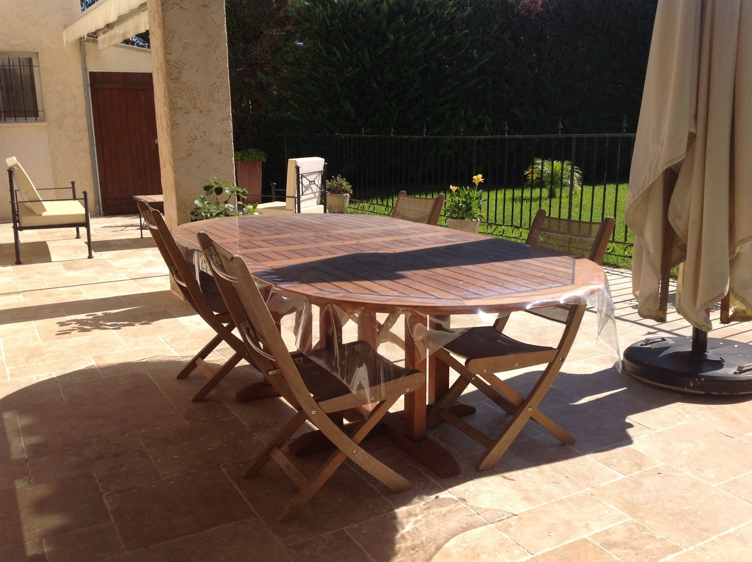 A round wooden table with four chairs, a small potted plant, and a metal fence in the background.