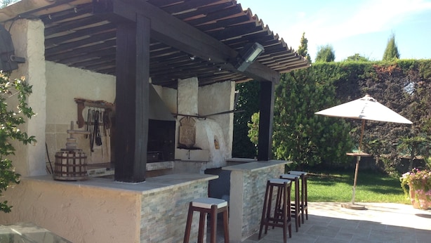 An outdoor kitchen area with a stone countertop, wooden stools, and a pergola overhead. - villa near cannes (Mougins)