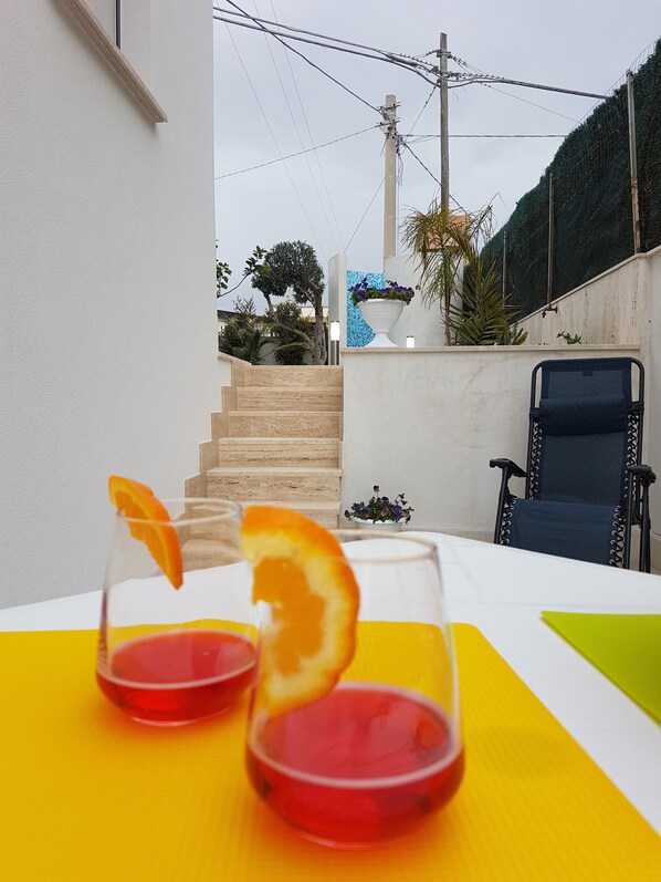 A table with two glasses of red beverage, a chair, and a staircase leading to a balcony with plants.