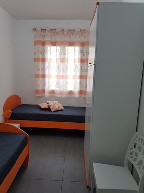A small, well-lit room with two beds, a chair, and a wardrobe.