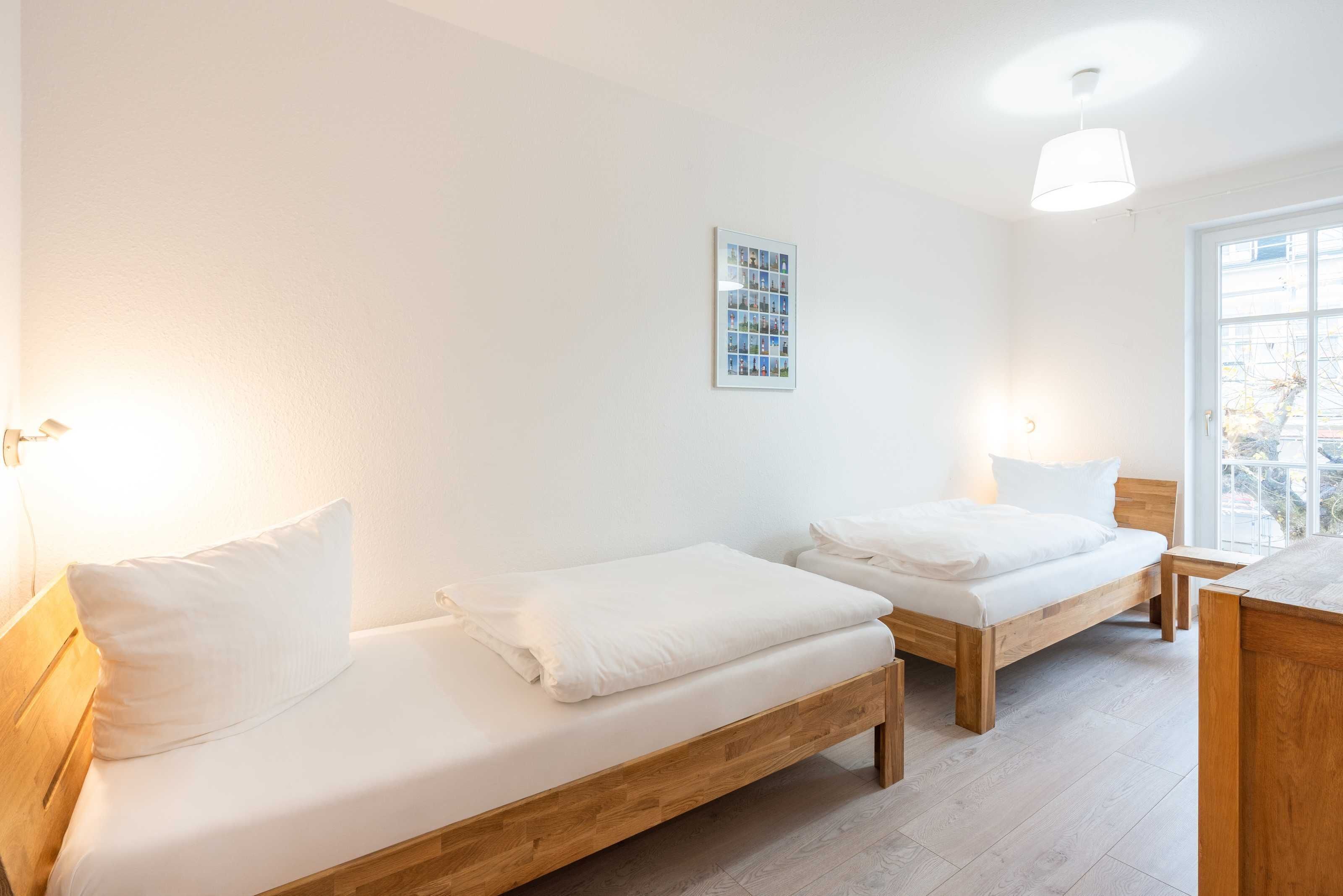 Una habitación con dos camas de madera, ropa de cama blanca, una foto enmarcada en la pared y una ventana con vistas.