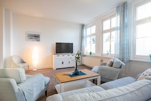 A modern living room with a sofa, armchair, coffee table, and a flat-screen TV on a white cabinet.