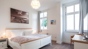 A bedroom with a bed, bedside table, lamp, and a window with curtains. - Starfish - villa on the beach (Heringsdorf)