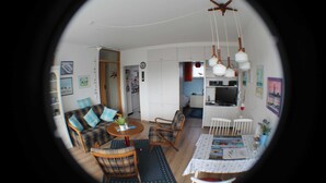 A living room with a sofa, chairs, a dining table, and a kitchen in the background. - Apartment seal (Wangerland)