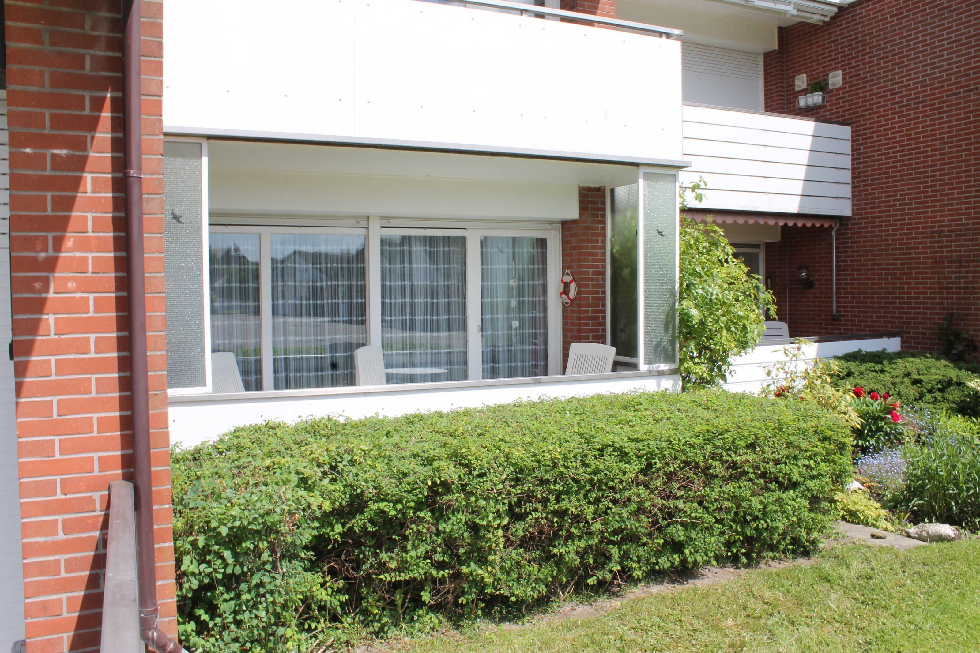 A residential building with a large windowed porch, a brick exterior, and a well-maintained garden.