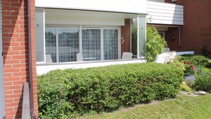 A residential building with a large windowed porch, a brick exterior, and a well-maintained garden. - Apartment seal (Wangerland)