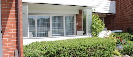 A residential building with a large windowed porch, a brick exterior, and a well-maintained garden.