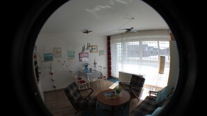 A living room with a round coffee table, two sofas, a dining table with chairs, and a large window with curtains. - Apartment seal (Wangerland)