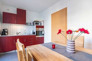 A modern kitchen with red cabinets, a wooden dining table, and a vase with flowers. - Sanddune - Villa on the beach (new build) (Heringsdorf)