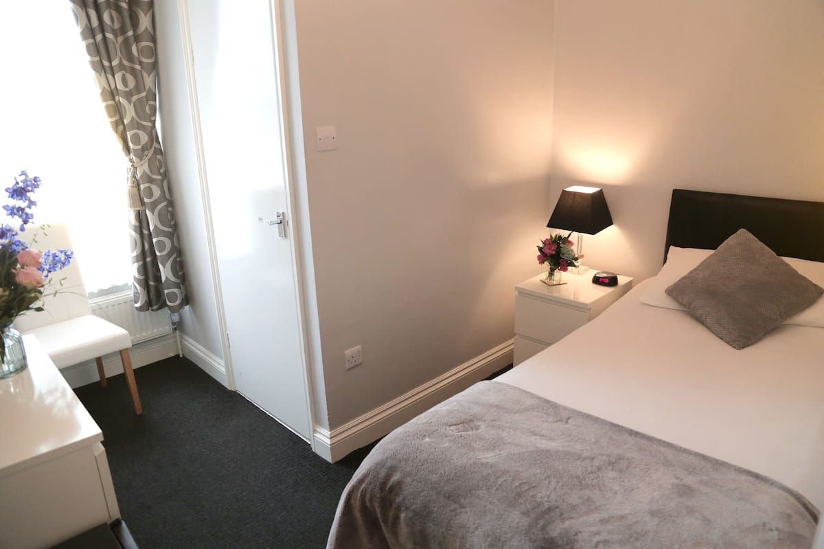 Una habitación de hotel con cama, mesita de noche, lámpara y un jarrón con flores.