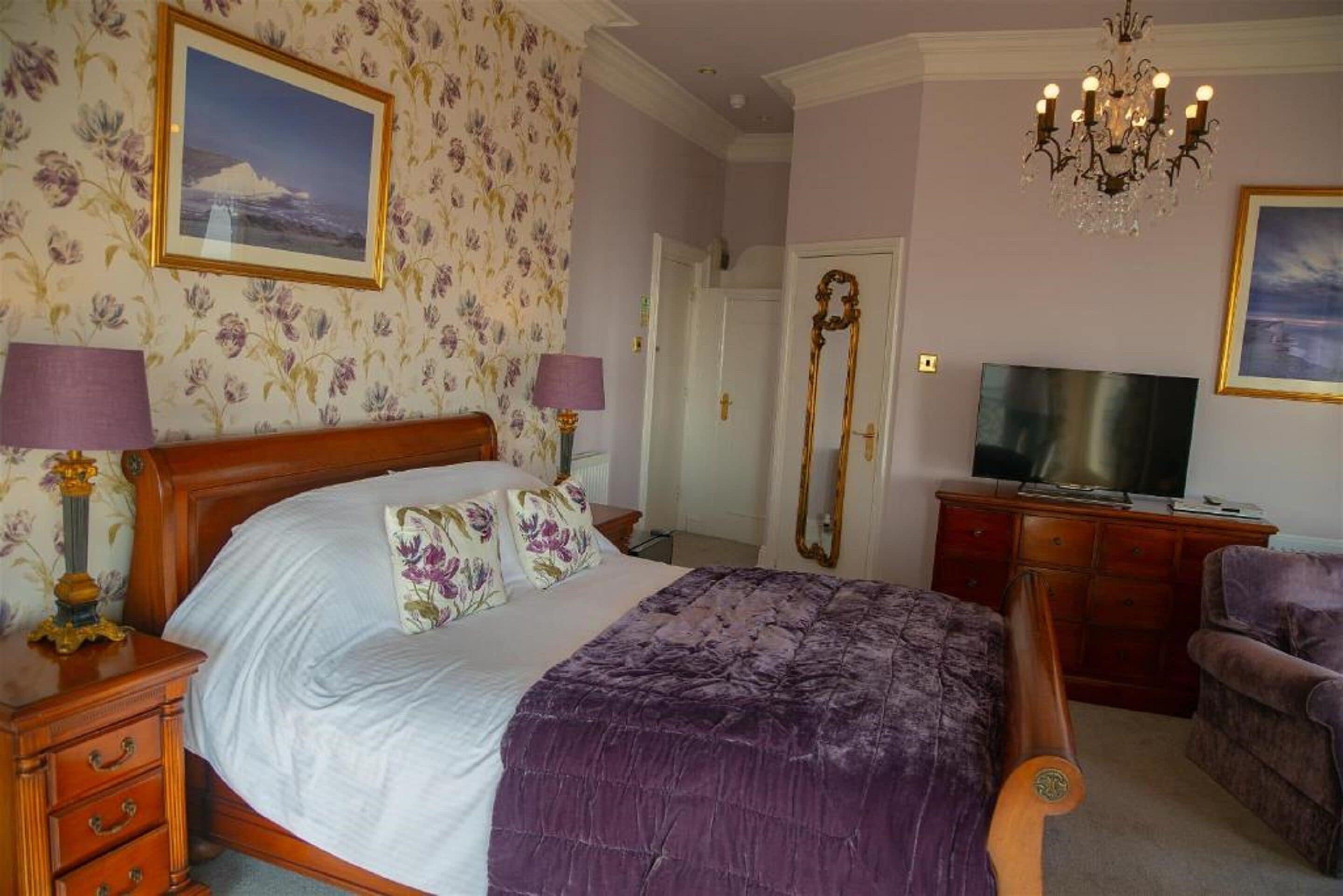 A bedroom with a large bed, a television, a dresser, and a mirror.
