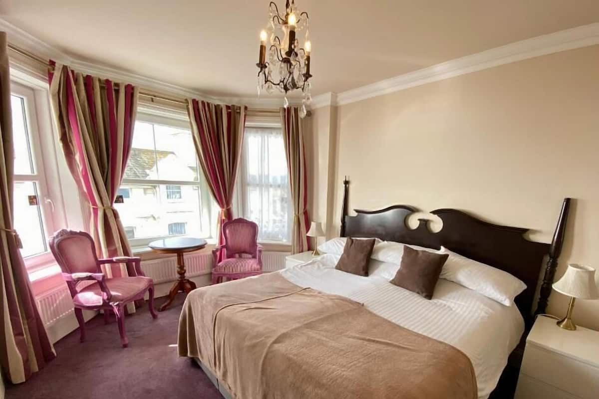 Una habitación de hotel con una cama grande, una silla, una mesita y un candelabro.