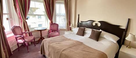 A hotel room with a large bed, a chair, a small table, and a chandelier.