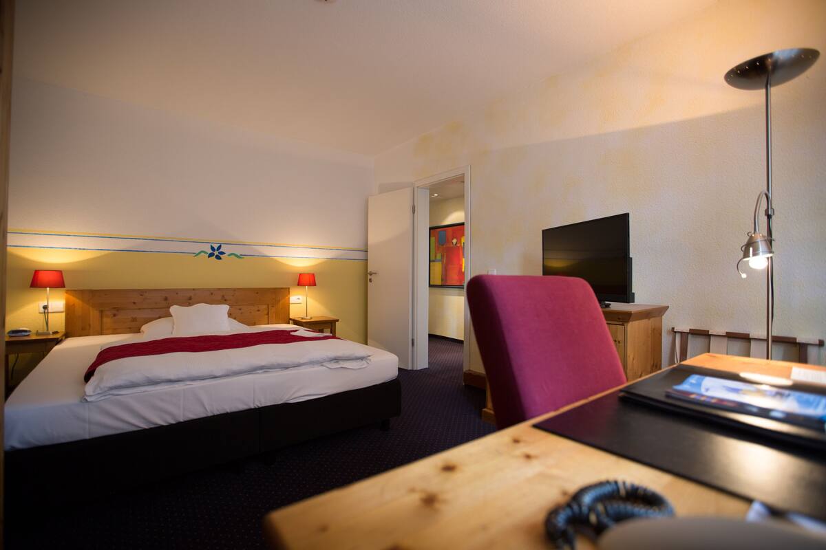 Ett hotellrum med en säng, sänglampor, ett skrivbord, en stol och en tv.