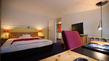 A hotel room with a bed, bedside lamps, a desk, a chair, and a TV.
