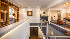 A modern interior with a central escalator, wooden shelving with various items, and a large abstract painting on the wall.