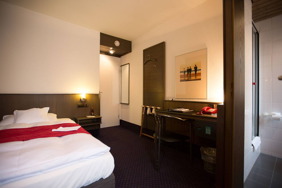 Ett hotellrum med en säng, ett skrivbord, en stol och en spegel.