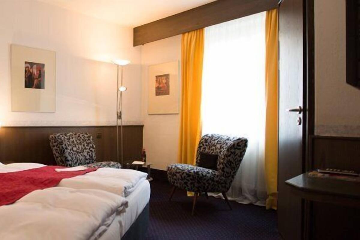 Ett hotellrum med en stor säng, två stolar, ett skrivbord och en tv.
