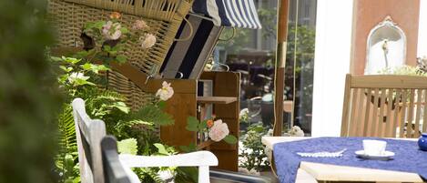 A wicker chair with a striped cushion, a wooden table with a blue tablecloth, and a white chair.