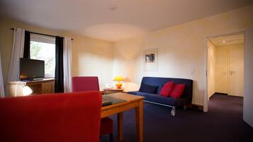 A room with a wooden table, red chair, blue sofa, and a TV on a desk.