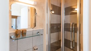 Ein modernes Badezimmer mit Duschkabine aus Glas, einer Ablagefläche für Toilettenartikel und einem großen Spiegel.