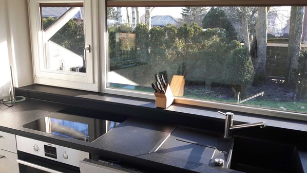 A kitchen with a black countertop, stainless steel sink, and a window with a view of a backyard.