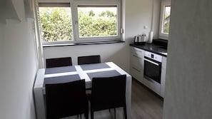 A small kitchen with a dining table and chairs, a stove, and a window with a view of greenery.
