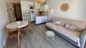 A compact living space with a kitchenette, a dining area, and a sofa with decorative pillows. - Cozy 2-Room Apartment, 250m from Beach, Terrace, Private Parking, Sleeps 4 (Port-la-Nouvelle)